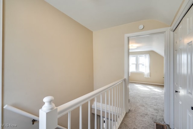 hallway featuring an upstairs landing, visible vents, carpet flooring, and vaulted ceiling