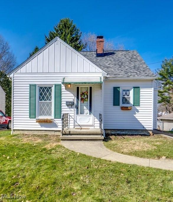 bungalow featuring board and batten siding, a front lawn, roof with shingles, and a chimney