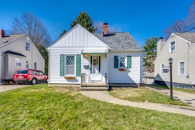 bungalow with board and batten siding, a chimney, a front yard, and roof with shingles