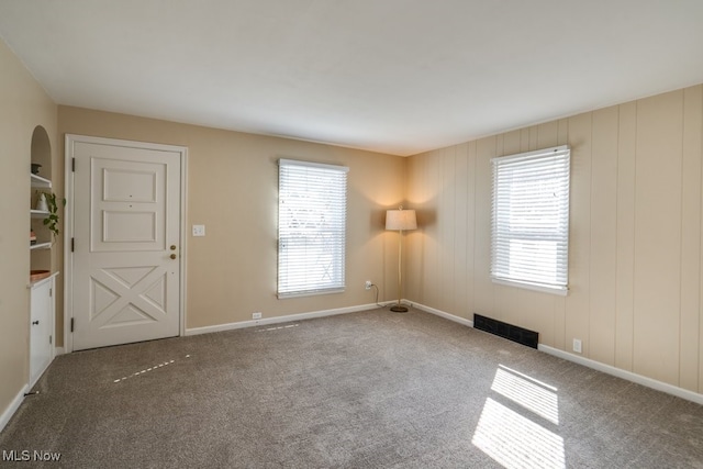 carpeted empty room featuring a wealth of natural light, visible vents, and baseboards