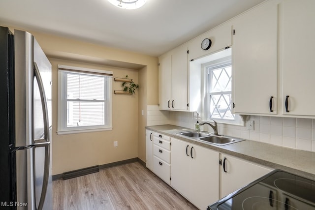 kitchen with tasteful backsplash, light wood-style flooring, freestanding refrigerator, electric range, and a sink