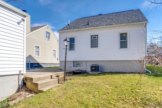 back of house featuring central air condition unit, a lawn, and a shingled roof