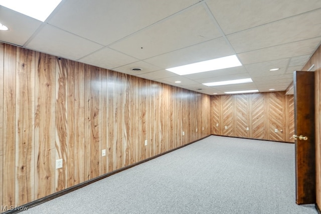 finished basement with wooden walls, visible vents, carpet, and a drop ceiling