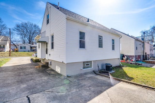 view of home's exterior with central AC unit, a yard, and roof with shingles