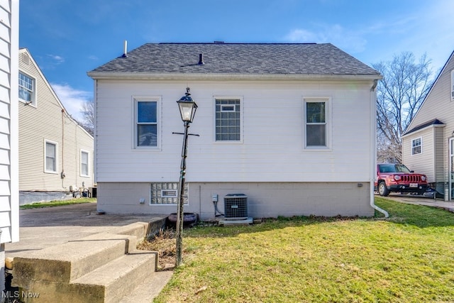 rear view of property with a lawn, cooling unit, and roof with shingles