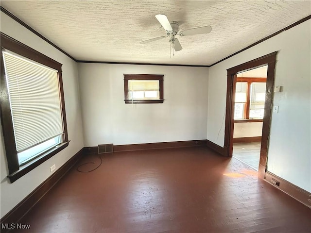 empty room with visible vents, wood finished floors, a textured ceiling, and ornamental molding