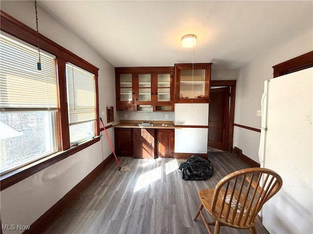 kitchen with baseboards, freestanding refrigerator, hanging light fixtures, dark wood-type flooring, and glass insert cabinets