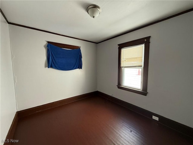 empty room featuring dark wood-type flooring, crown molding, and baseboards