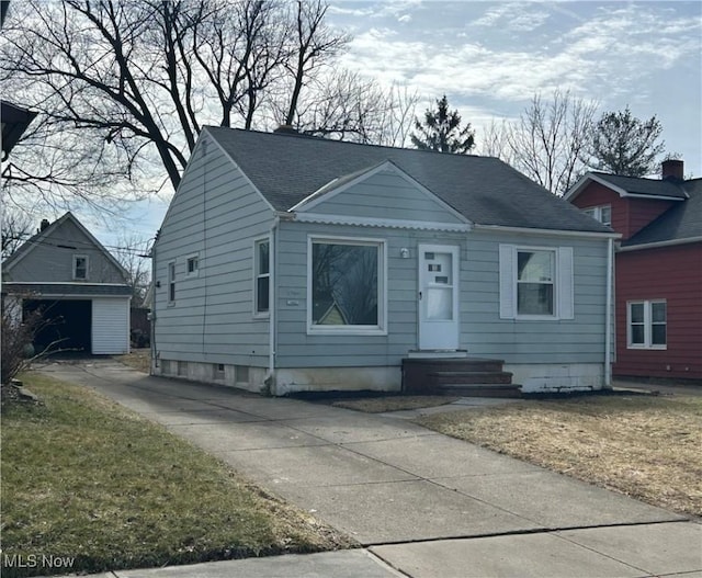 bungalow-style house with concrete driveway, a detached garage, an outdoor structure, and a shingled roof