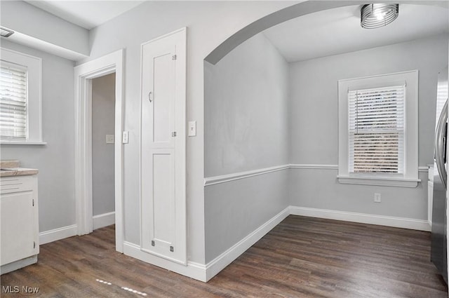 unfurnished dining area featuring baseboards, arched walkways, and dark wood-style flooring