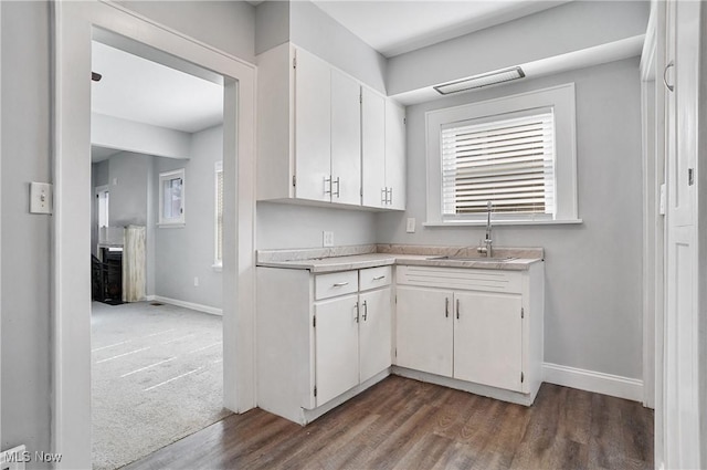 kitchen featuring baseboards, light countertops, wood finished floors, white cabinets, and a sink