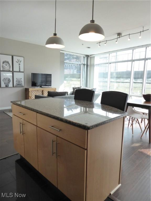 kitchen featuring track lighting, decorative light fixtures, a kitchen island, dark stone counters, and a wall of windows