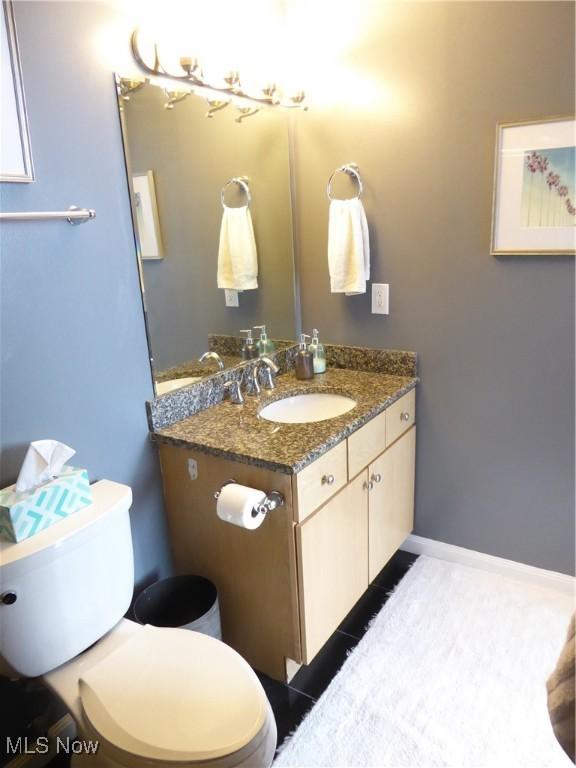 half bathroom with tile patterned flooring, toilet, vanity, and baseboards