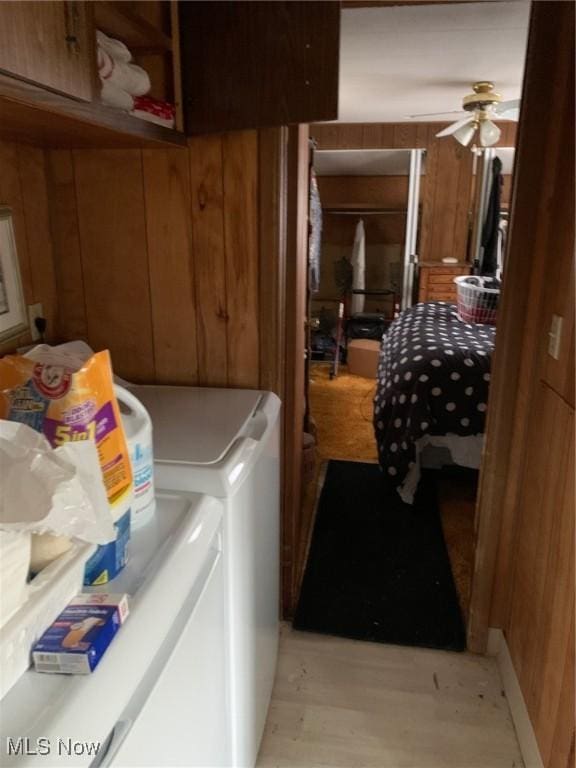 washroom with light wood finished floors, wooden walls, washer and dryer, and a ceiling fan