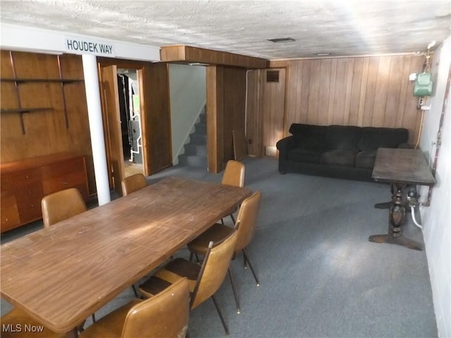 dining area with visible vents, wooden walls, carpet, stairway, and a textured ceiling