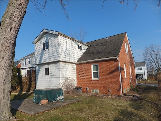 back of house featuring brick siding, a lawn, and roof with shingles