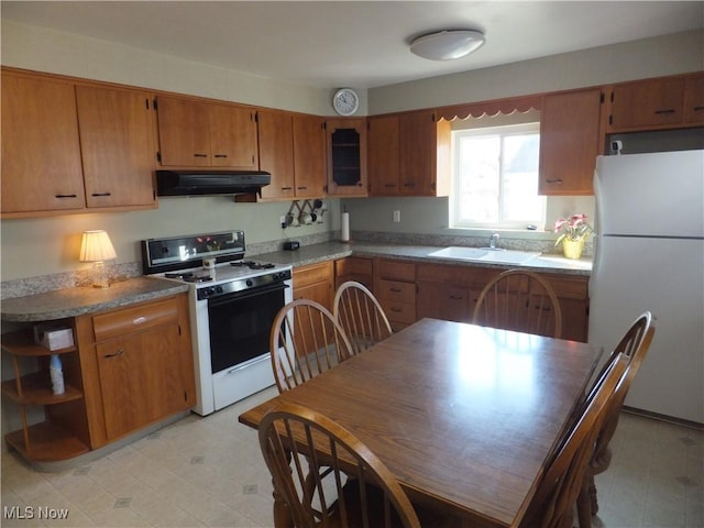 kitchen featuring under cabinet range hood, light floors, brown cabinetry, white appliances, and a sink