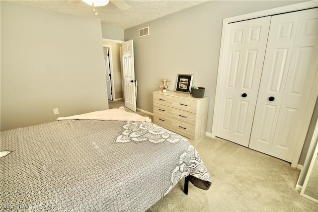 bedroom featuring visible vents, a textured ceiling, a closet, light colored carpet, and ceiling fan