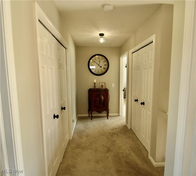 hallway featuring light colored carpet and baseboards