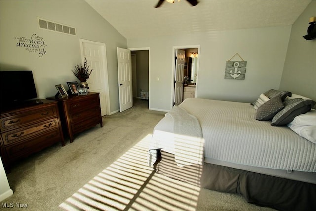 bedroom with visible vents, baseboards, light colored carpet, lofted ceiling, and ensuite bathroom