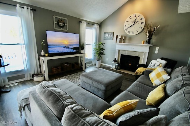 living area featuring visible vents, baseboards, a fireplace with flush hearth, vaulted ceiling, and wood finished floors