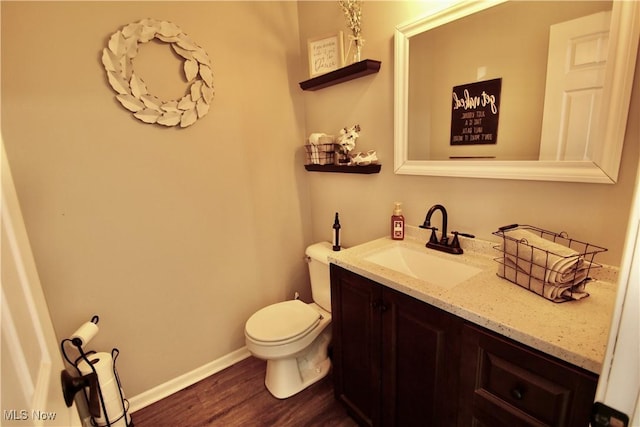 half bathroom with vanity, toilet, wood finished floors, and baseboards