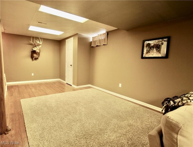 finished basement featuring visible vents, light wood-style flooring, and baseboards