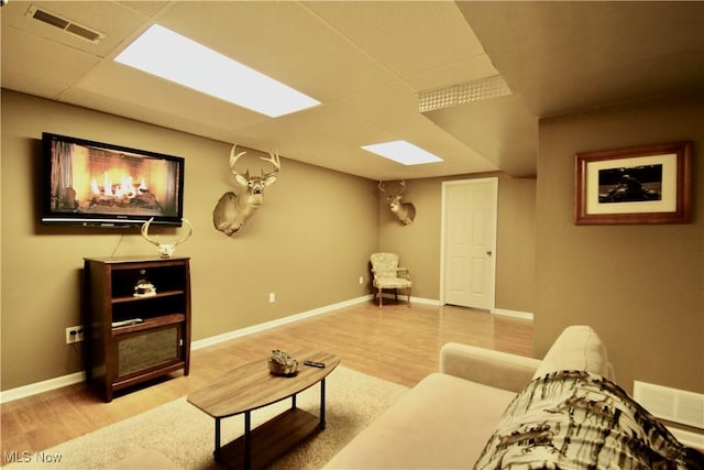 living area featuring a paneled ceiling, visible vents, baseboards, and wood finished floors