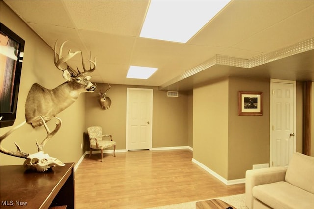 living area with a paneled ceiling, baseboards, and light wood finished floors