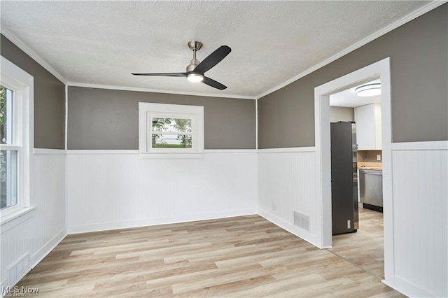 empty room with light wood-type flooring, visible vents, a textured ceiling, and wainscoting