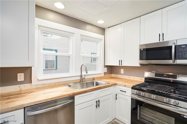 kitchen with appliances with stainless steel finishes, wooden counters, white cabinetry, and a sink