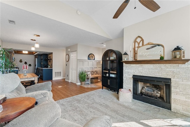 living room featuring a stone fireplace, lofted ceiling, visible vents, and ceiling fan