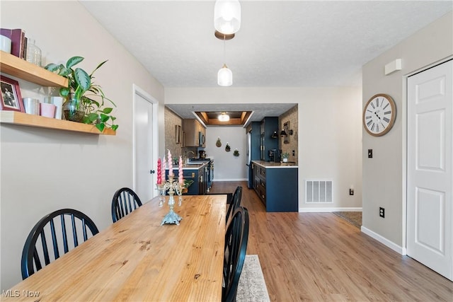 dining space with visible vents, a textured ceiling, baseboards, and wood finished floors