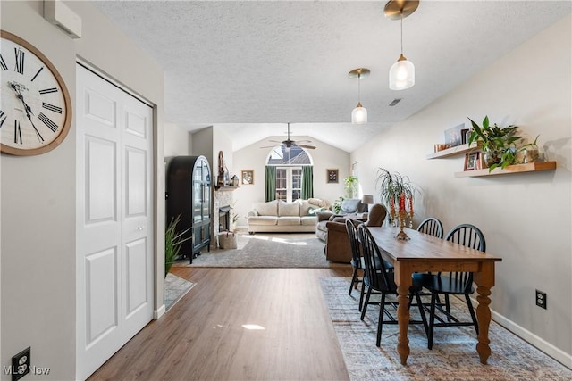 dining space with lofted ceiling, a textured ceiling, wood finished floors, and a fireplace