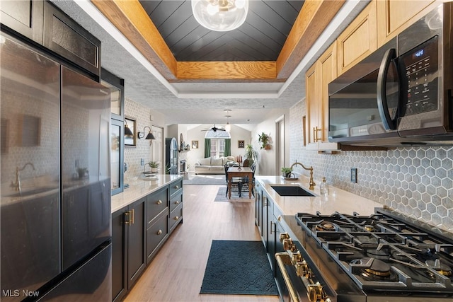 kitchen featuring tasteful backsplash, open floor plan, stainless steel appliances, a raised ceiling, and a sink