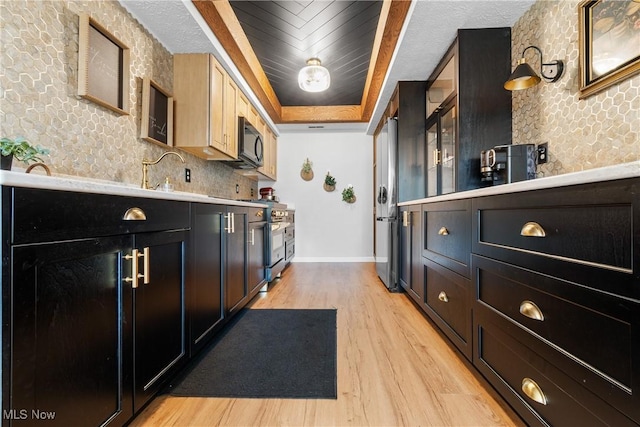 kitchen featuring high end range, baseboards, light wood-style flooring, black microwave, and a raised ceiling