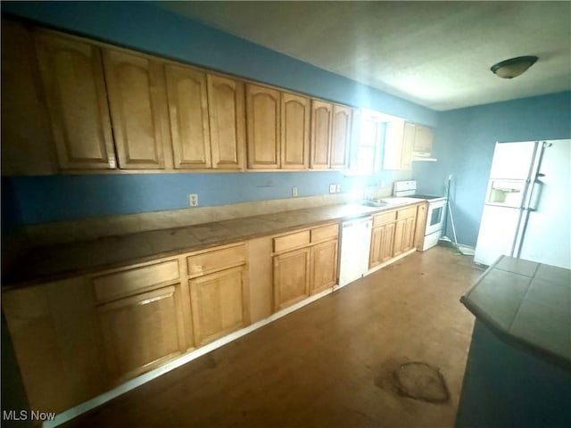 kitchen featuring tile counters, white appliances, light brown cabinetry, and a sink