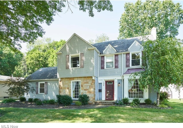 view of front of home with a front yard, stone siding, roof with shingles, and a chimney