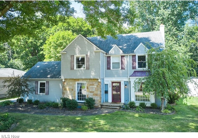 view of front facade with a chimney, a front yard, and a shingled roof