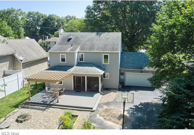 rear view of property with a shingled roof, fence, a wooden deck, driveway, and an attached garage