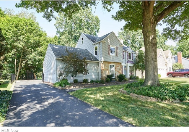 view of front of house with aphalt driveway, stone siding, and a front lawn