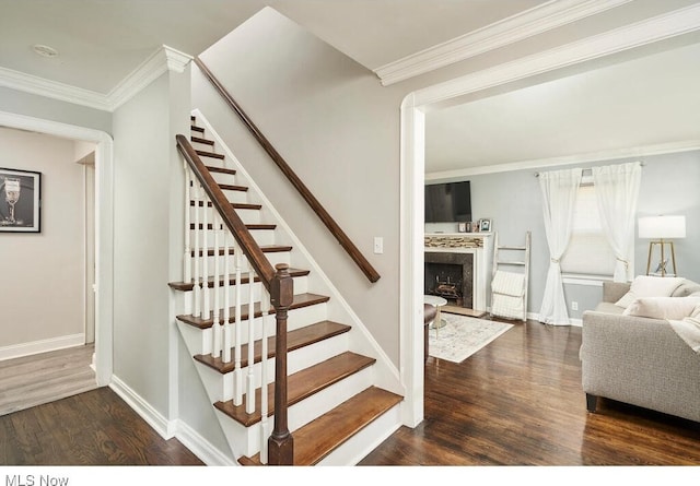 stairs featuring baseboards, wood finished floors, a fireplace, and ornamental molding