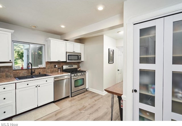 kitchen with light wood-type flooring, a sink, tasteful backsplash, stainless steel appliances, and white cabinets