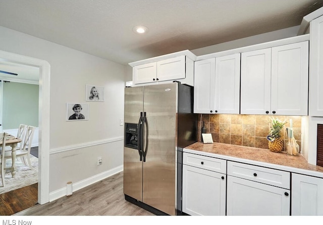 kitchen with light wood finished floors, light countertops, white cabinets, stainless steel fridge, and backsplash