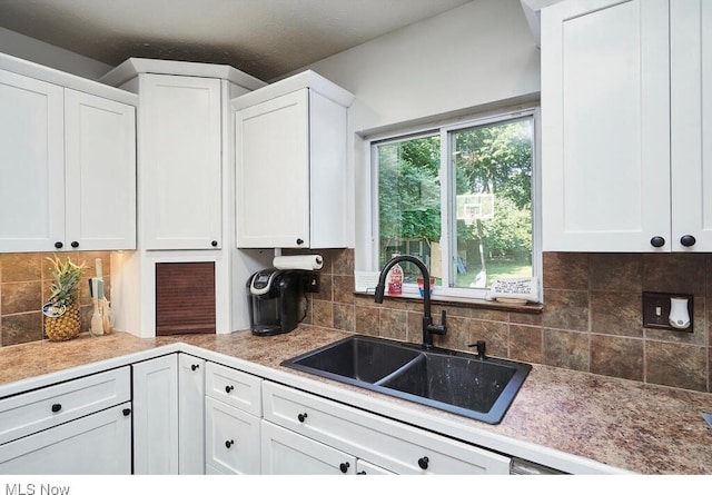 kitchen with light countertops, white cabinets, backsplash, and a sink