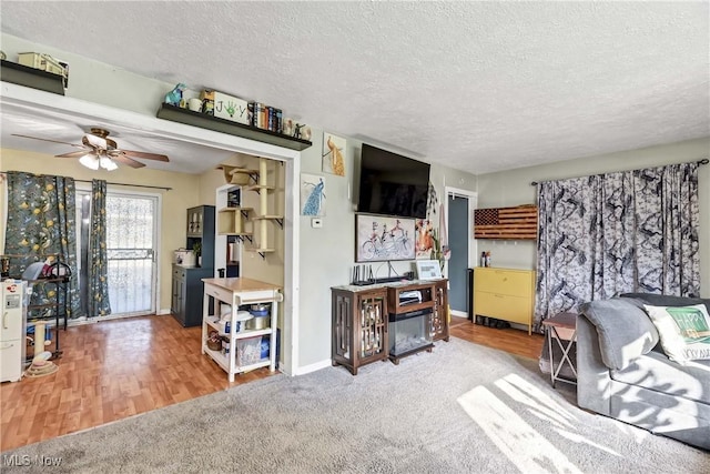 living room featuring baseboards, a textured ceiling, a ceiling fan, and wood finished floors