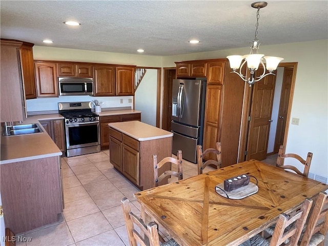 kitchen featuring a kitchen island, light tile patterned flooring, a sink, appliances with stainless steel finishes, and a notable chandelier