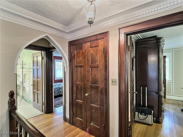 hall with arched walkways, a textured ceiling, ornamental molding, and light wood finished floors