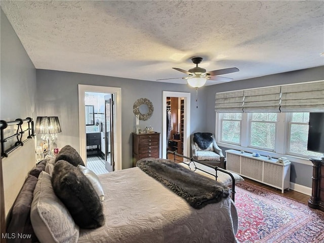 bedroom featuring a ceiling fan, wood finished floors, radiator heating unit, a spacious closet, and connected bathroom