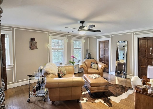 living area with ceiling fan, hardwood / wood-style floors, ornamental molding, and a decorative wall